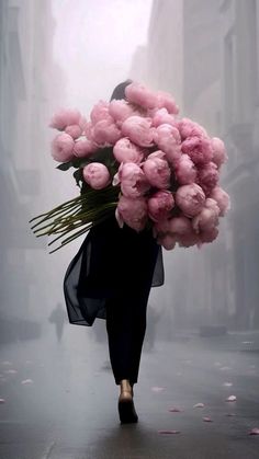 a woman walking down the street carrying a bunch of pink flowers on her back,