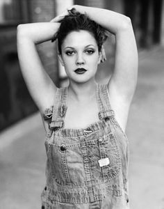 a black and white photo of a woman in overalls with her hands on her head