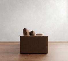 a brown couch sitting on top of a wooden floor next to a white wall in an empty room