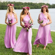 three beautiful women in long dresses standing next to each other on the grass near water