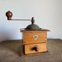 an old fashioned coffee grinder sitting on top of a wooden table next to a wall