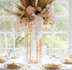 a tall vase with flowers and feathers on top of a table in front of a window