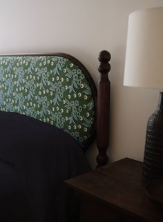 a bed with a green headboard next to a night stand and lamp on the nightstand