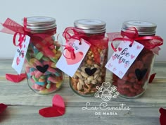 three jars filled with different types of candies and hearts on top of a wooden table