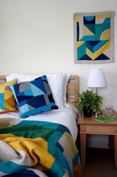 a bed with colorful blankets and pillows in a bedroom next to a small wooden table