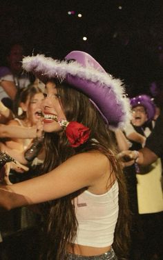 a woman wearing a purple hat and red rose in her mouth is surrounded by other people