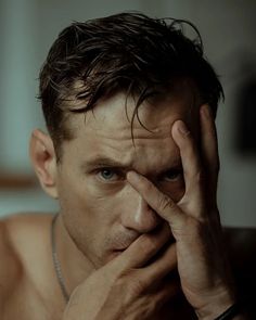 a shirtless man holding his hands to his face while looking at the camera with an intense look on his face