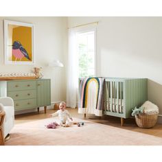 a baby sitting on the floor next to a crib in a room filled with furniture