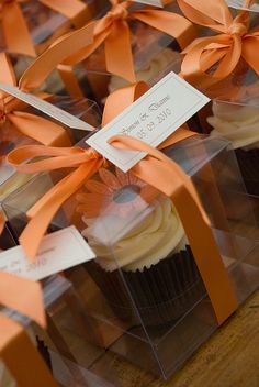 cupcakes in clear boxes with orange ribbons tied around the edges and tags on them