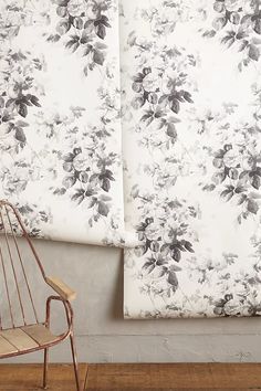 a chair sitting in front of a wall with floral curtains