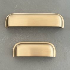 two brass cabinet handles on a gray wall, one has an oval handle and the other has a rectangular handle