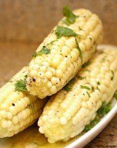 grilled corn on the cob with mustard and parsley in a white bowl