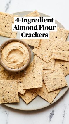 crackers on a plate with a bowl of hummus and some sort of dip