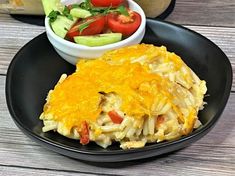 a black plate topped with an omelet next to a bowl of salad