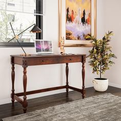 a desk with a laptop on it in front of a painting and potted plant