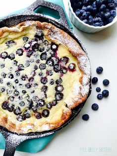 a blueberry pie with powdered sugar on top and berries around the edges, in a cast iron skillet