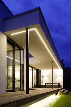 an exterior view of a modern house at night with lights on the side and grass in front