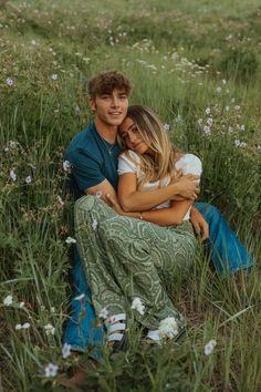 a man and woman are sitting in the grass with their arms wrapped around each other