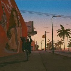 a man riding a bike down a street next to a tall red wall and palm trees