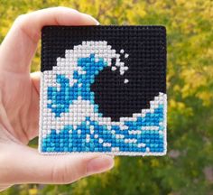 a hand holding up a beaded square with an image of a wave on it