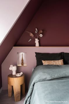 a bed sitting under a slanted ceiling next to a table with a vase on it