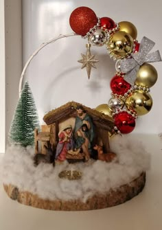 a nativity scene is displayed on top of a tree stump with ornaments around it