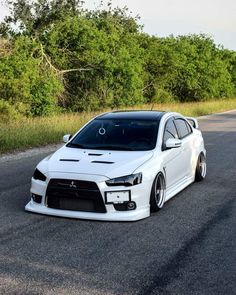 the white car is parked on the side of the road in front of some trees