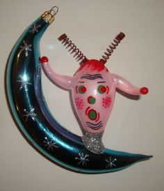 an ornament hanging from the side of a crescent with a pink and green face on it