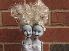 two dolls are standing next to each other in front of a brick wall and one has blonde hair