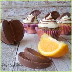 cupcakes with chocolate frosting and orange slices on a white wooden table next to a brick wall