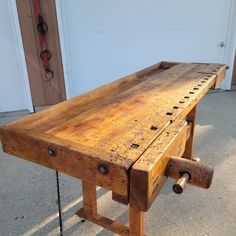 a wooden bench sitting on top of a cement floor next to a garage door with tools in it