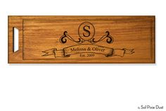 a wooden cutting board with an engraved monogrammed name and scroll on the front