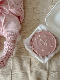 a pink cookie sitting on top of a bed next to a white container and blanket