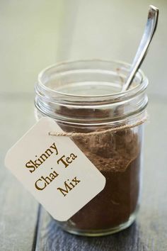 a glass jar with a spoon in it on a wooden table next to a label that says skinnyy chai tea mix