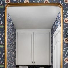 a bathroom with blue and white wallpaper has a gold framed mirror over the sink