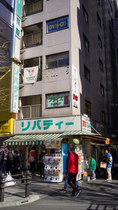 people walking on the street in front of a tall building with japanese writing and advertisements