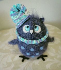 a knitted owl with blue eyes and a hat on its head sitting on a bed