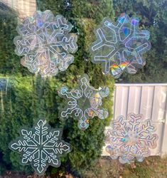 four snowflakes are shown in the window with green bushes behind them and one is upside down