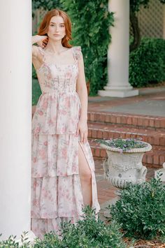 a woman in a floral dress leaning against a pillar