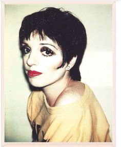 a woman with black hair and red lipstick posing for a photo in front of a white wall