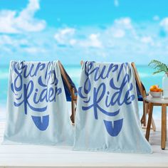 two beach towels with the words surf your ride printed on them sitting next to an ocean view