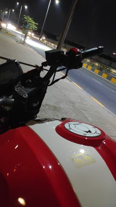 the handlebars on a red and white motorcycle are visible at night in front of an empty street