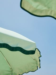 two green and white umbrellas flying in the air with blue sky behind them on a sunny day