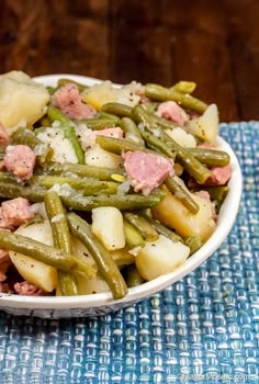 a white bowl filled with green beans and potatoes on top of a blue place mat