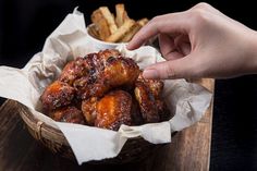 a basket filled with fried chicken wings next to french fries on top of a wooden cutting board