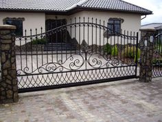 an iron gate in front of a house with stone walkways and brick pavers