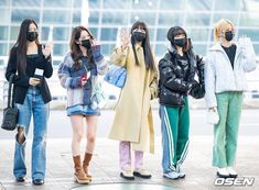 four young women wearing face masks and standing on the sidewalk in front of an airport