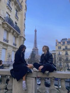 two women sitting on a ledge in front of the eiffel tower