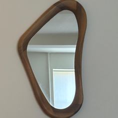 a wooden mirror hanging on the wall next to a white wall with a window in it