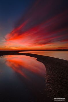 the sky is reflected in the still water at sunset on the beach, with red and orange clouds